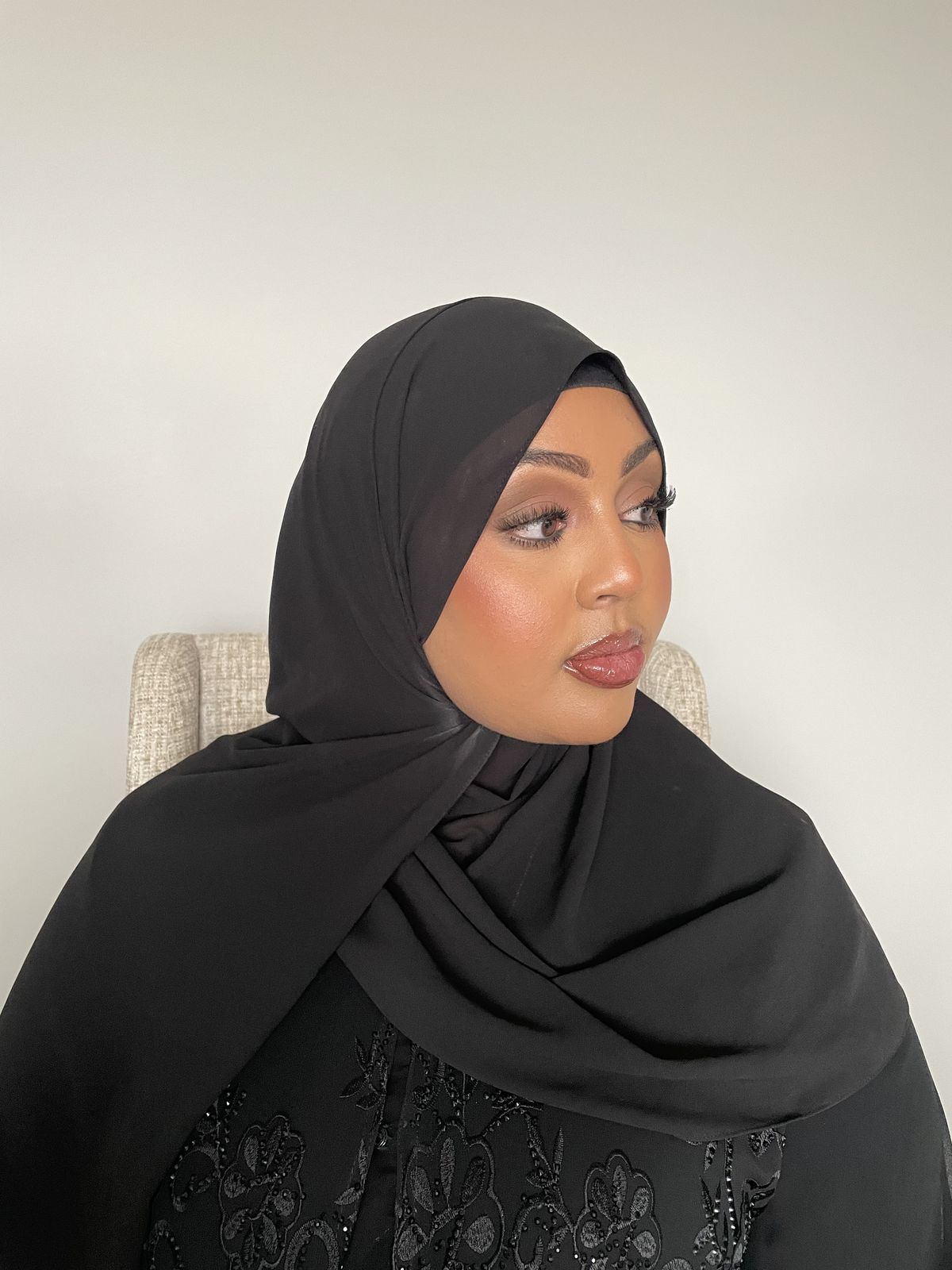 Client in black hijab with sculpted soft glam, glancing to the side